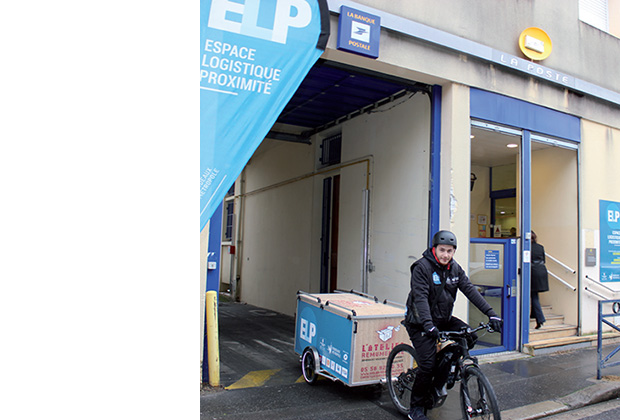 Photo de l'espace logistique de proximité de Bordeaux, avec un livreur qui en sort, conduisant un vélo avec remorque